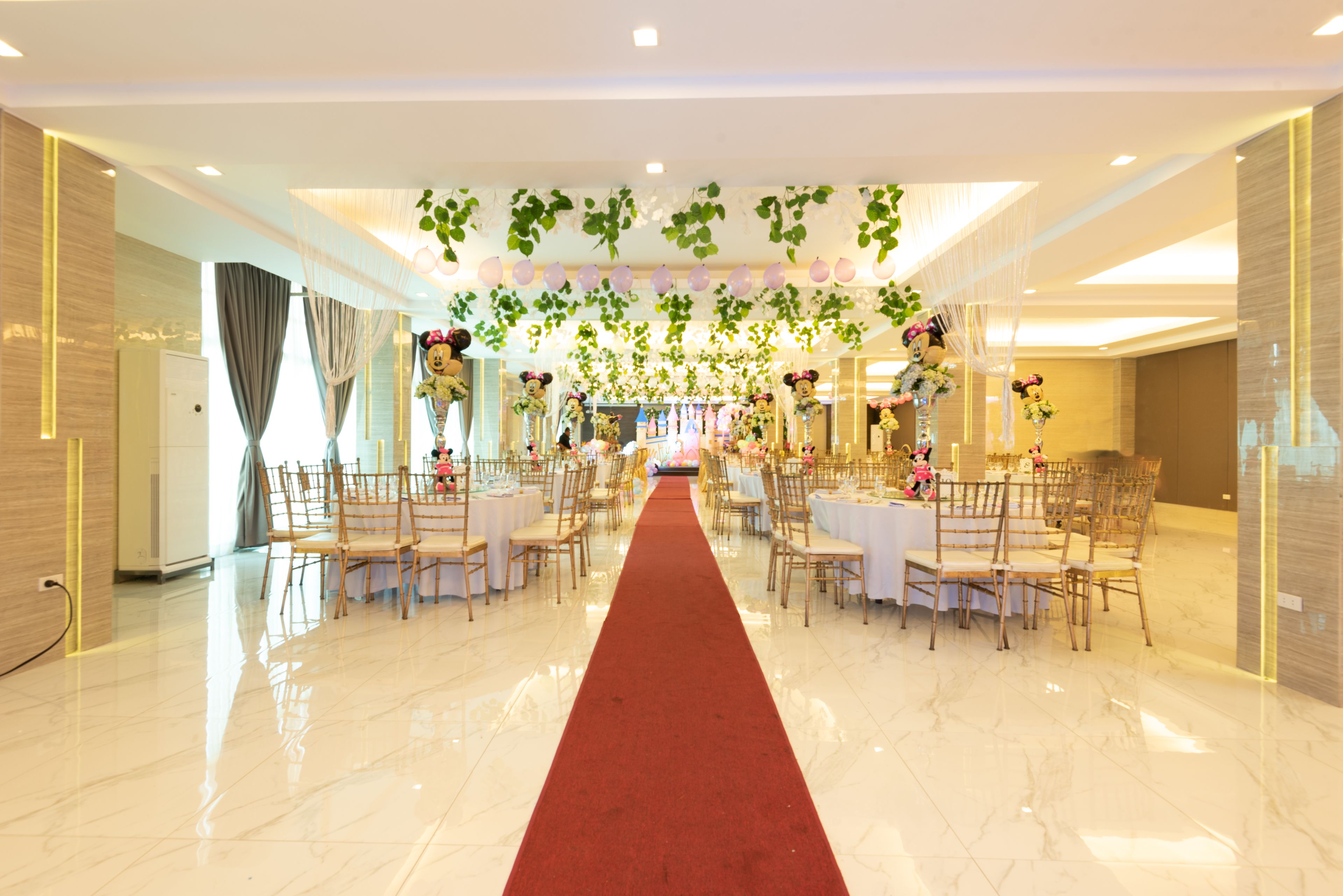 Un amplio salón de banquetes con piso de mármol pulido, una alfombra roja que conduce al área de comedor y mesas dispuestas para un evento formal.