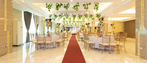 Un amplio salón de banquetes con piso de mármol pulido, una alfombra roja que conduce al área de comedor y mesas dispuestas para un evento formal.
