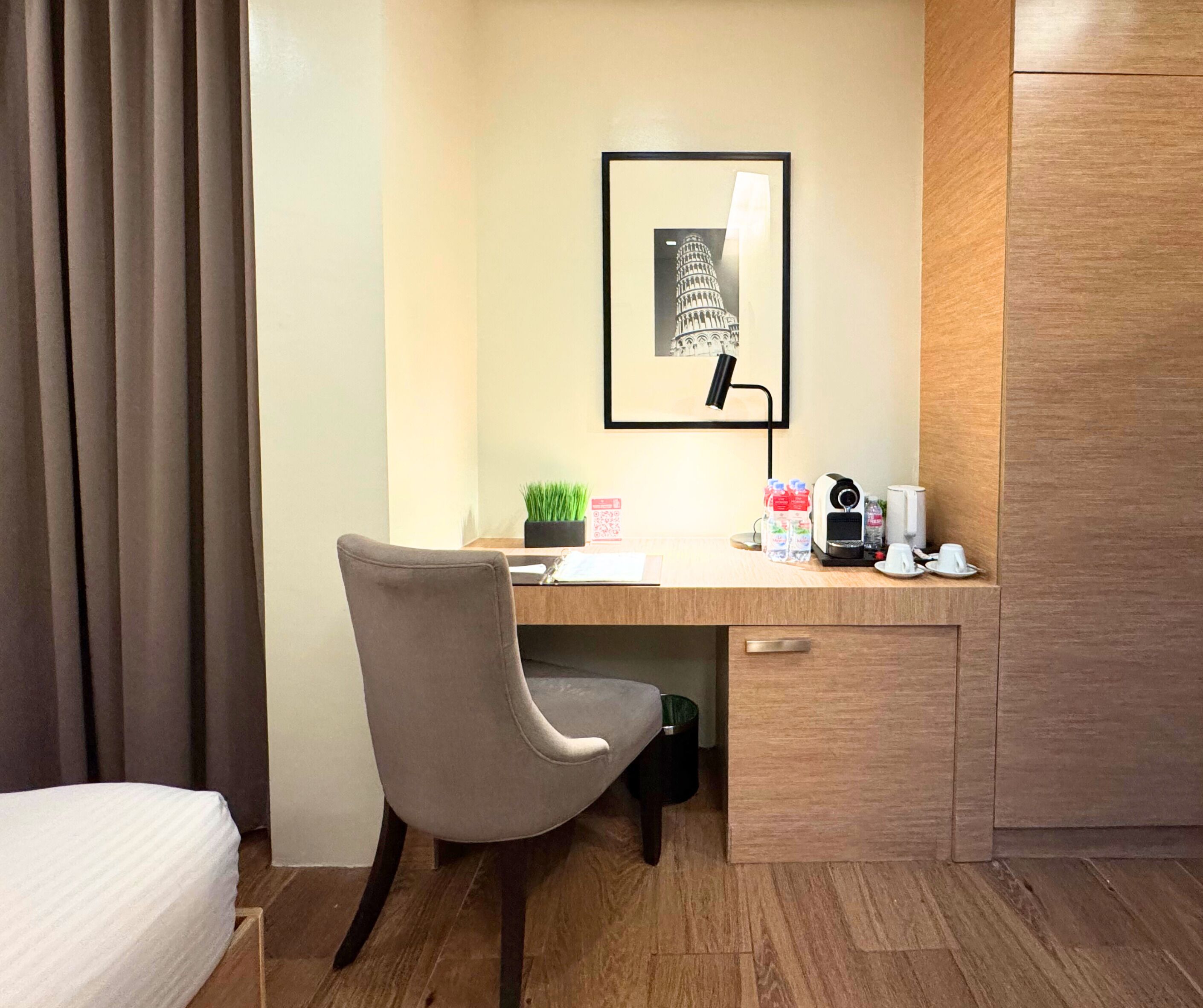 Habitación de hotel con cama, un escritorio con silla, un cuadro enmarcado en la pared y un armario de madera.