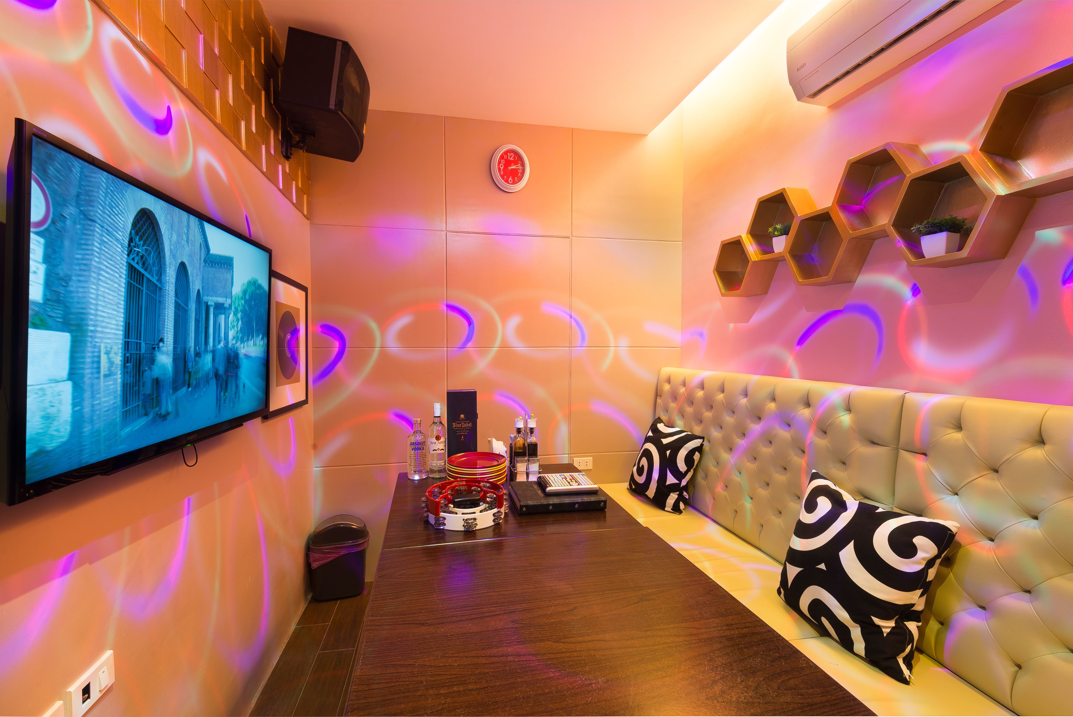 Een moderne zithoek met een flatscreen televisie, een bank met gestreepte kussens en hexagonale wandplanken.