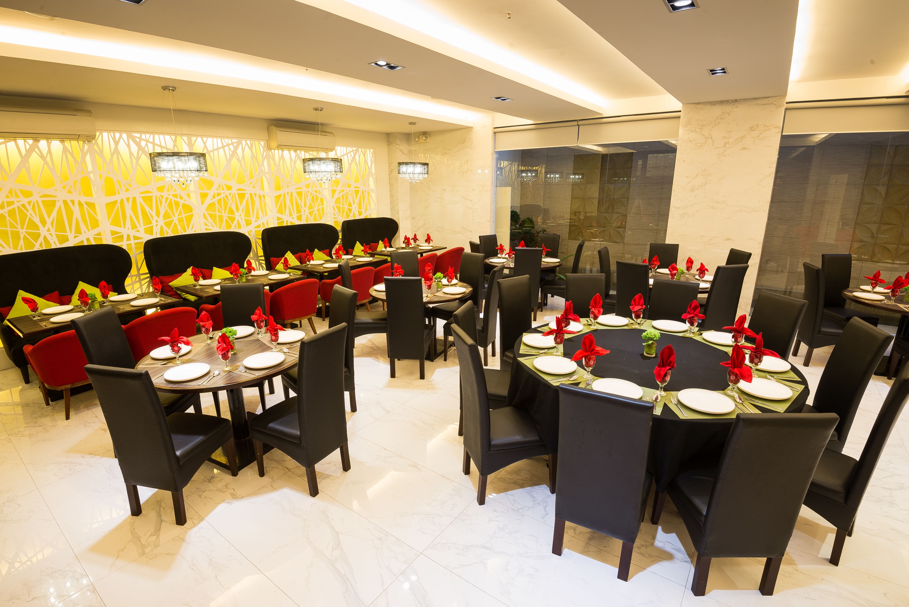 A restaurant with multiple round tables, black chairs, and red cushions.
