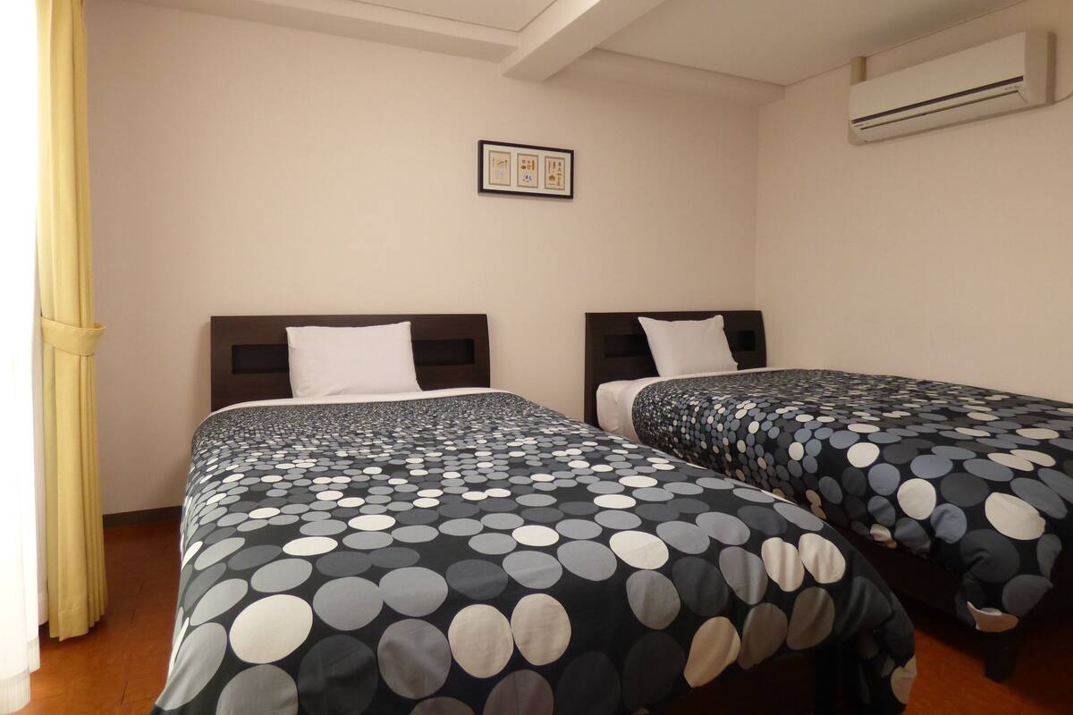 A hotel room with two beds, each with a polka dot bedspread, a framed picture on the wall, and an air conditioning unit.