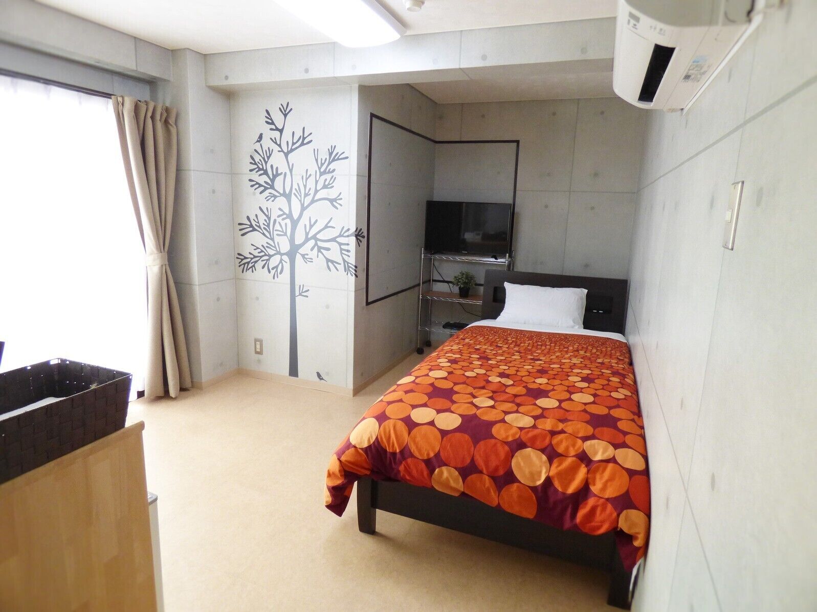 A hotel room with a bed, a TV, a wall-mounted air conditioner, and a window with curtains.