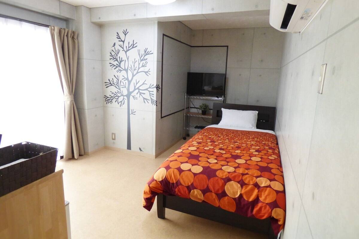 A hotel room with a bed, a TV, a wall-mounted air conditioner, and a window with curtains.