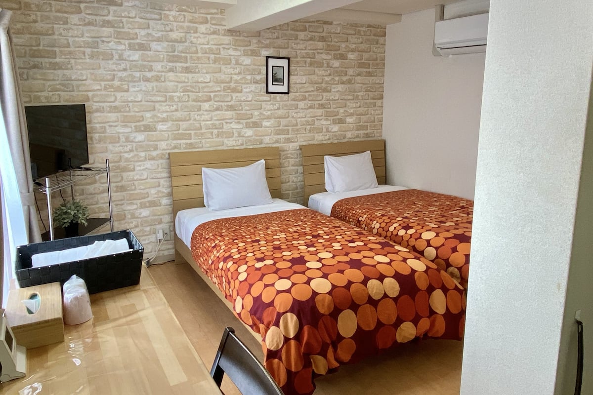 A room with two beds, a TV, a brick wall, and a picture on the wall.