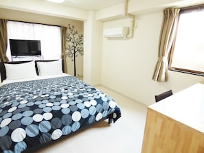 Una habitación de hotel con cama, televisión, escritorio y ventana con cortinas.