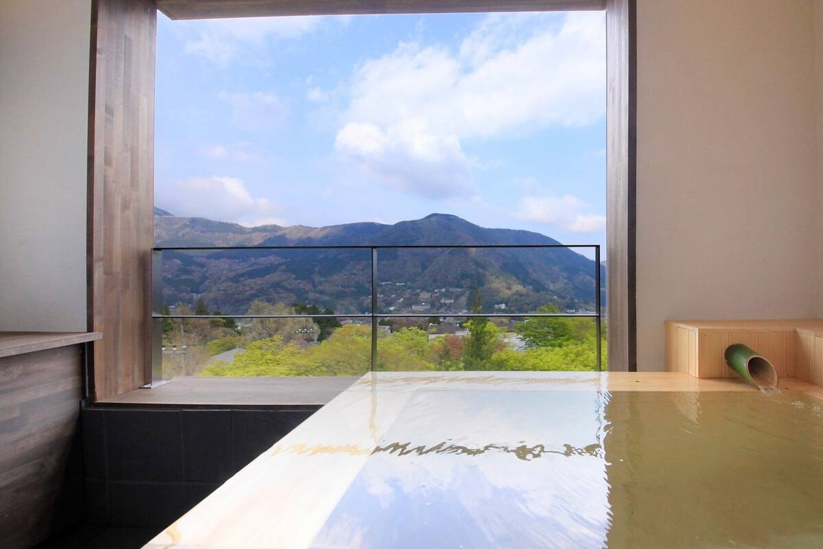 A modern bathroom with a large window, a wooden bench, and a bathtub.