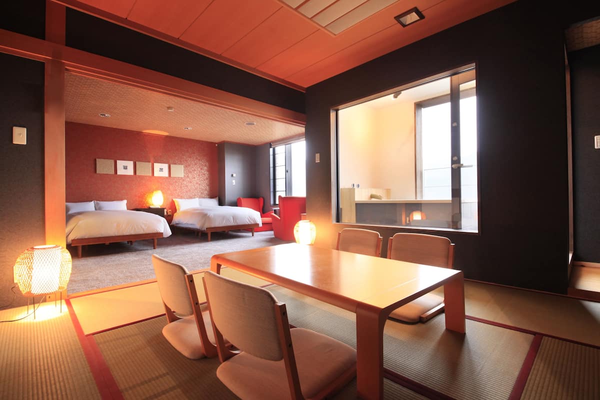 A hotel room with a bed, a dining table, chairs, and a large window.