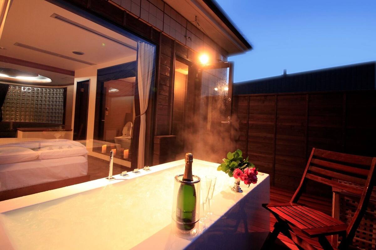 A hot tub with a bottle of champagne, a glass, and a vase of flowers.