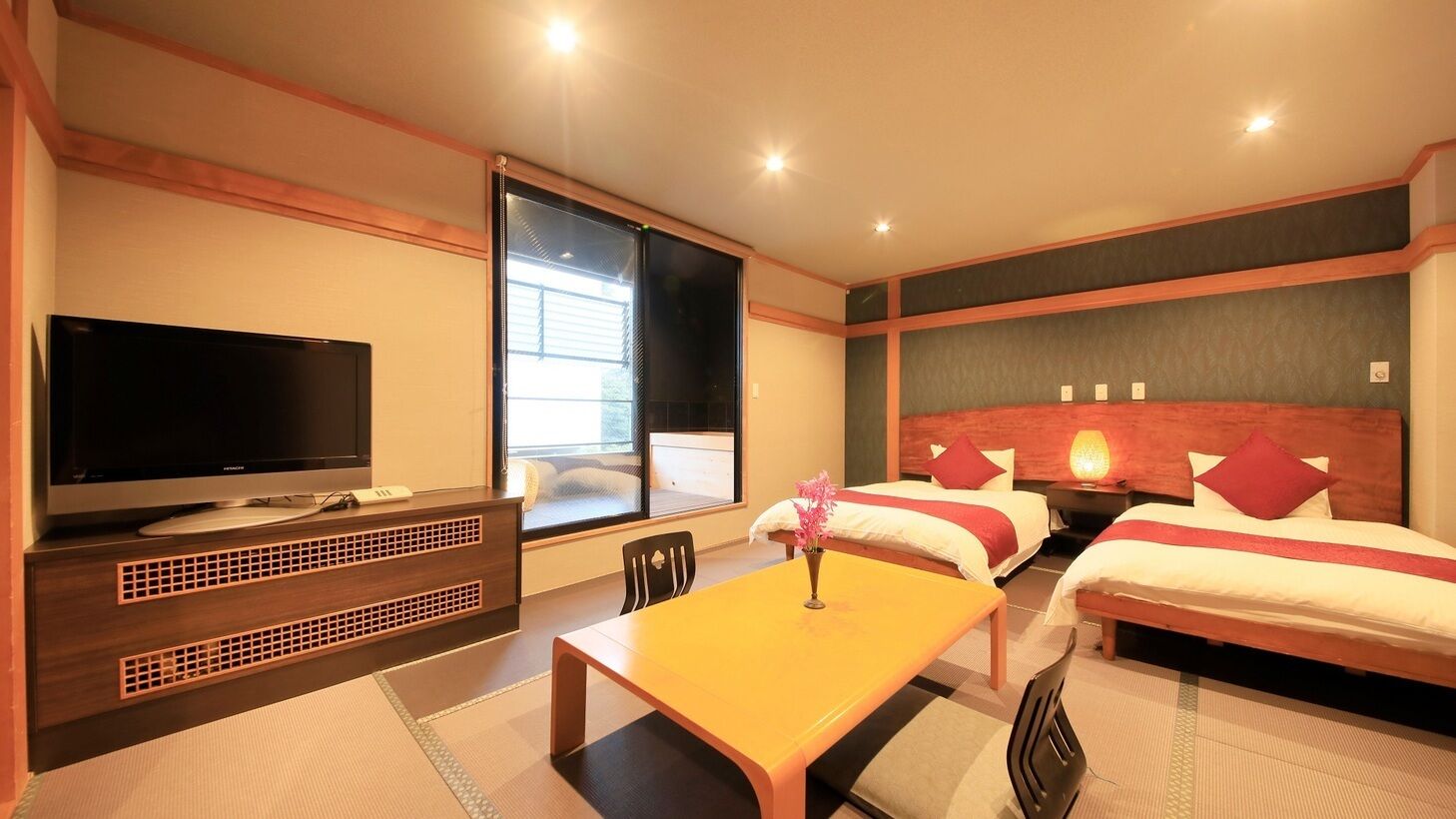 Een hotelkamer met een televisie, een eettafel, twee bedden en een raam.