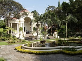 Un edificio clásico con columnas, una fuente y un jardín cuidado con palmeras y un estanque.