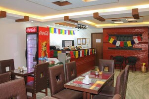 Un restaurante con cabinas y mesas, un refrigerador de Coca-Cola, una barra con menú y banderas coloridas.