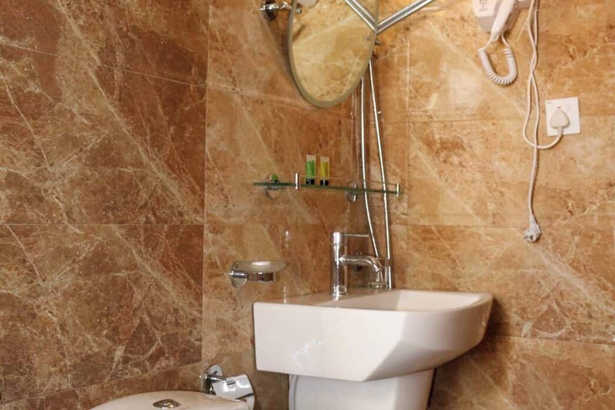 Ein Badezimmer mit Marmorwand, Toilette in Weiß, Waschbecken, Handbrause und einem an der Wand montierten Fön.