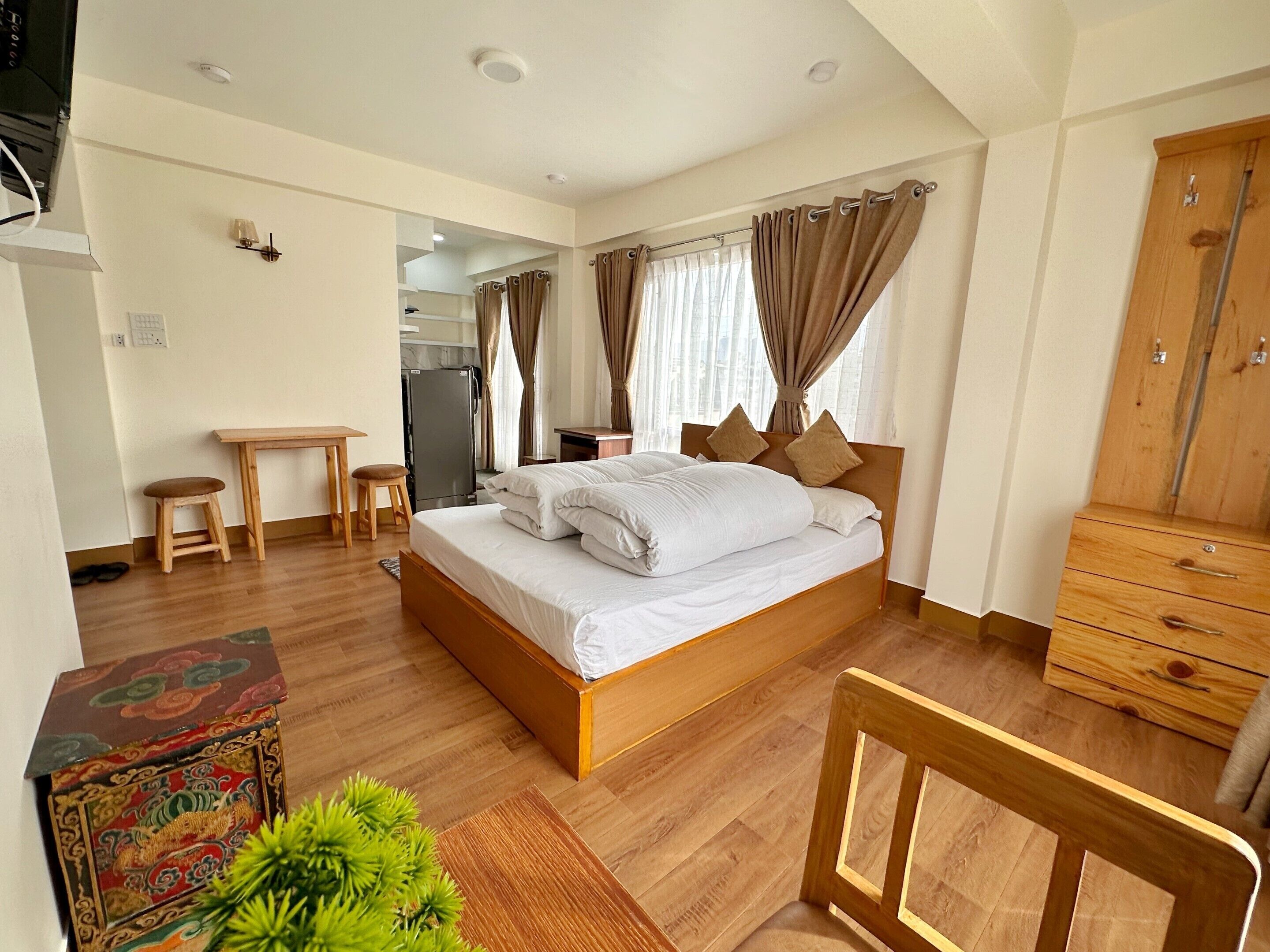 A bedroom with a wooden bed, a desk, a chair, a dresser, and a small plant.