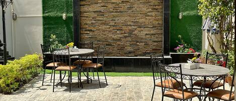 An outdoor patio with stone flooring, two round tables with chairs, and a decorative wall with a stone pattern.