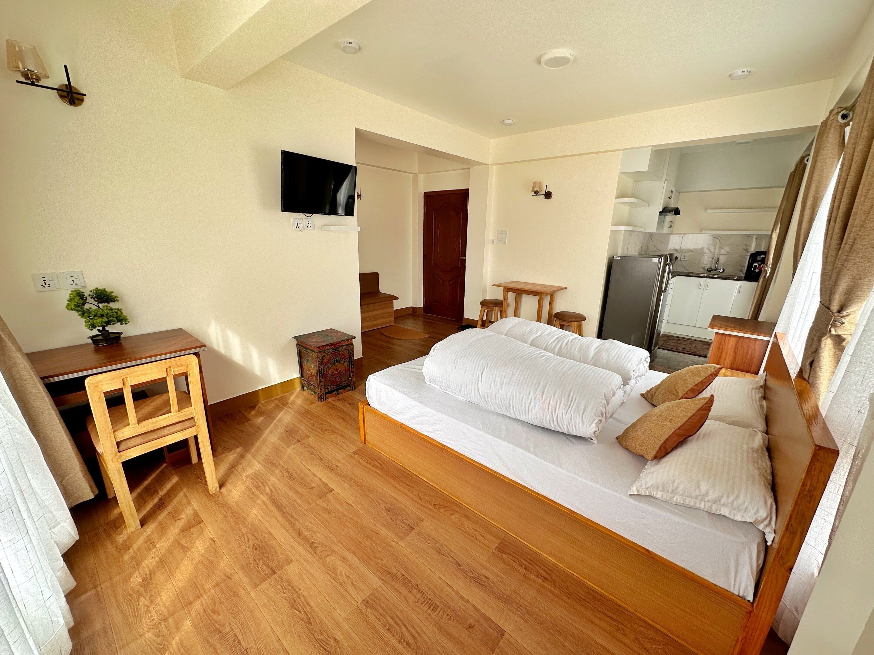 A bedroom with a bed, bedside tables, a desk, a chair, a television, and a small table with a plant.
