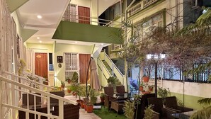 A multi-level indoor space with a staircase, wicker furniture, potted plants, and artificial grass. - Shakya House (Lalitpur)