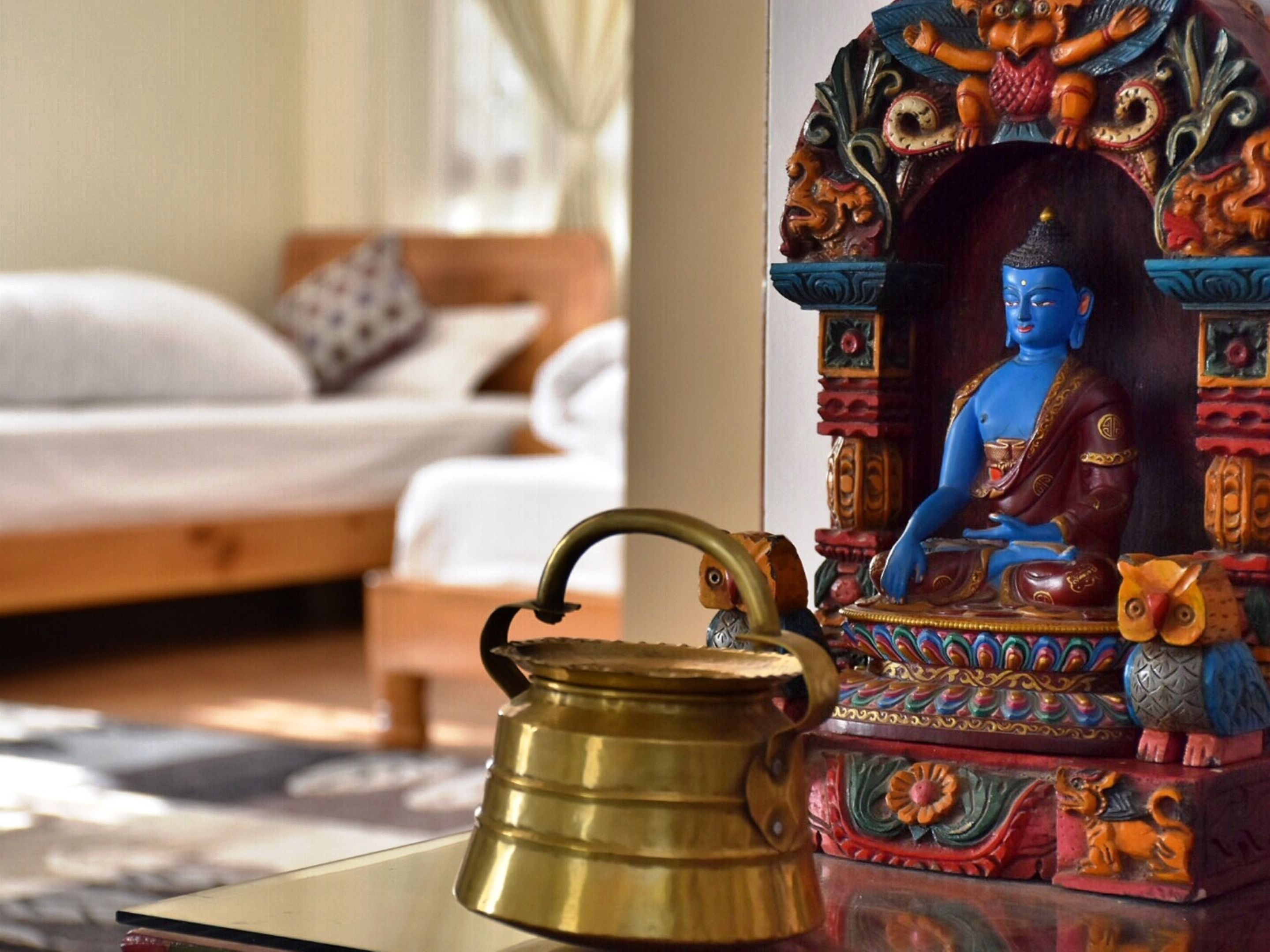 A room with a bed, a decorative Buddha statue, and a brass teapot on a table.