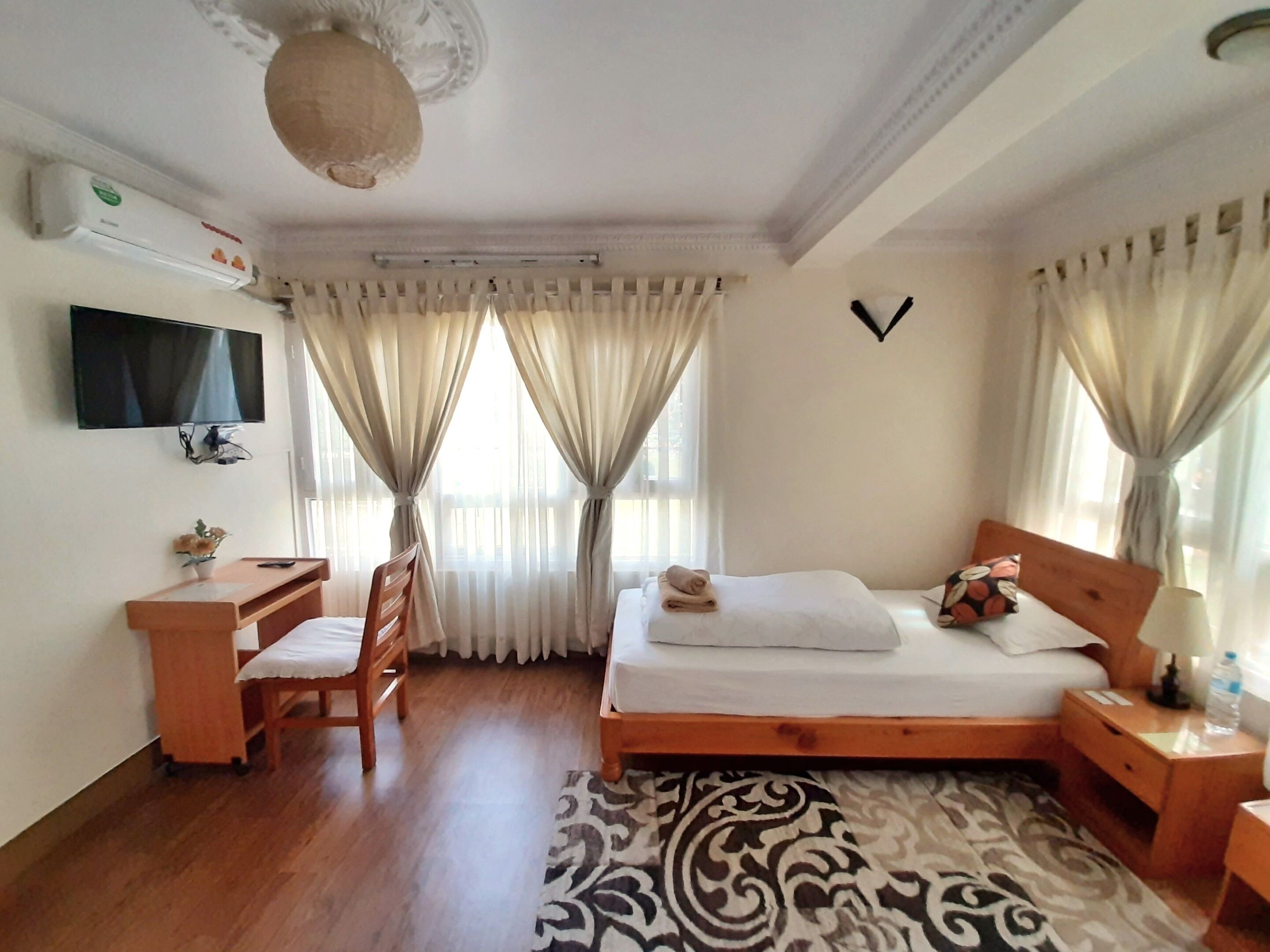 A hotel room with a bed, a desk, a chair, a television, and a window with curtains.