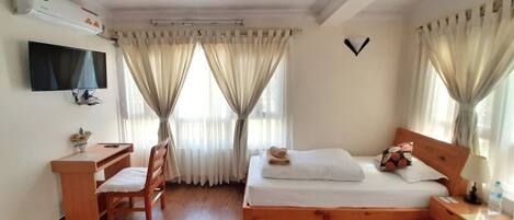 A hotel room with a bed, a desk, a chair, a television, and a window with curtains.