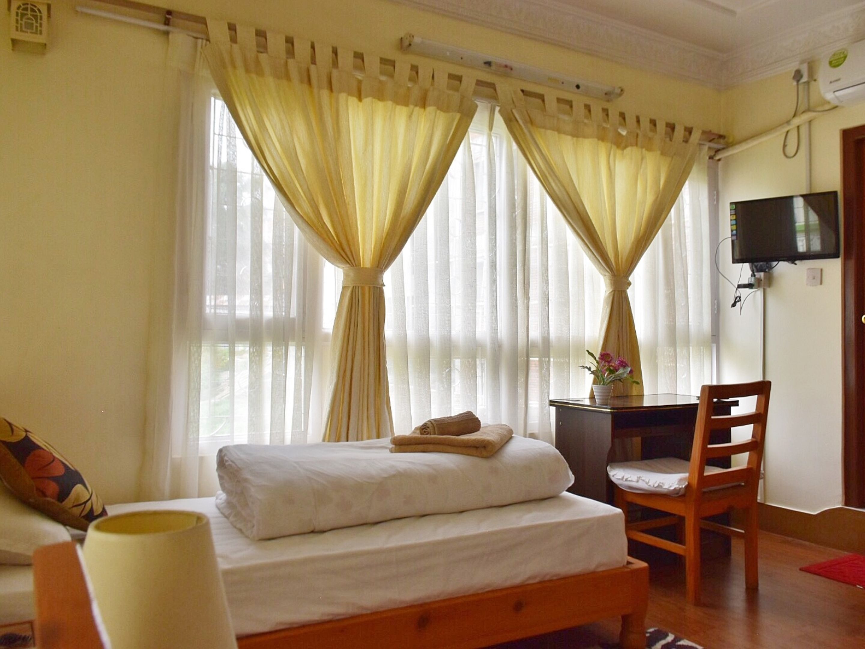 A hotel room with a bed, a desk, a chair, and a television on the wall.