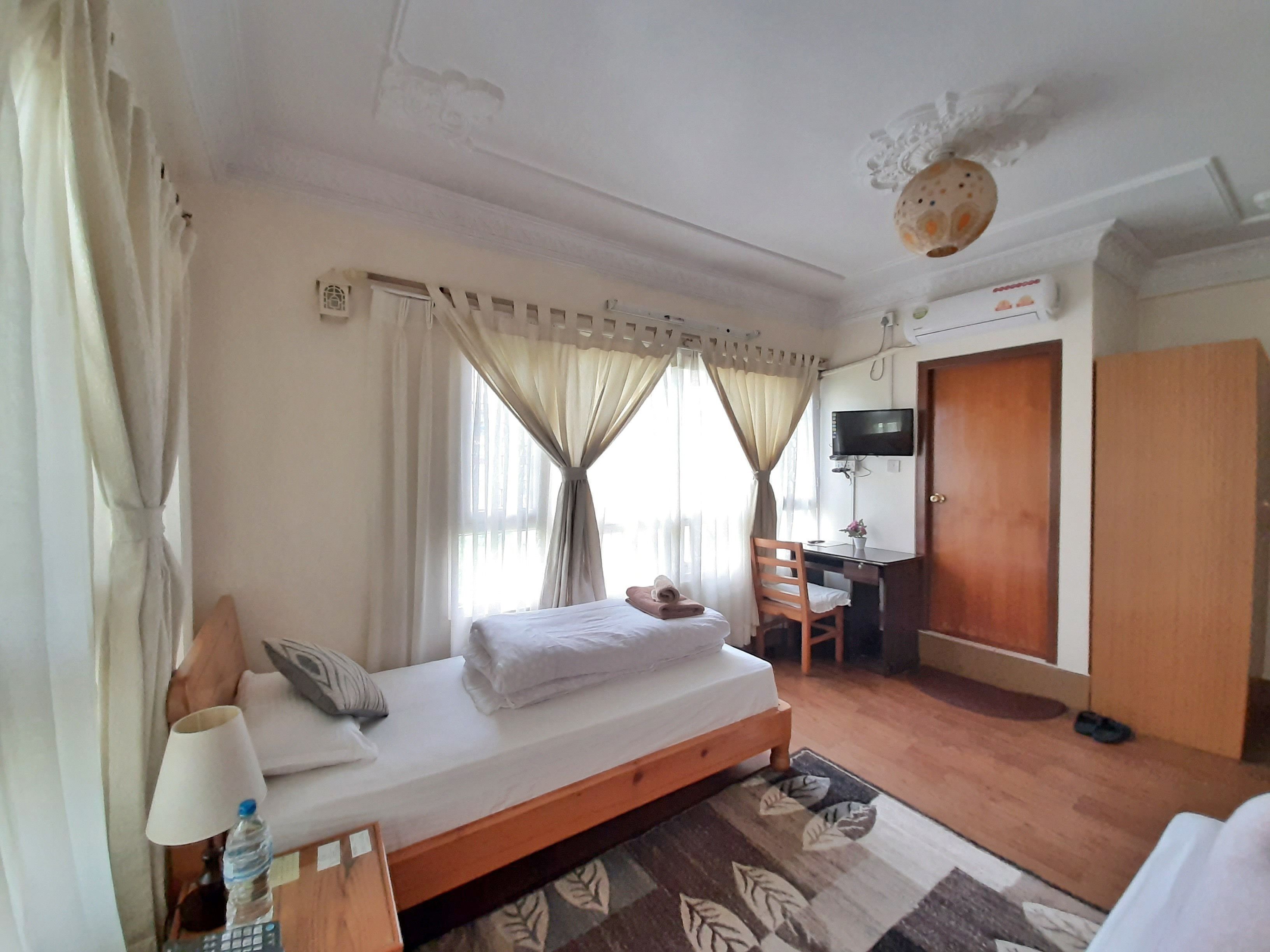 A hotel room with a bed, a desk, a chair, a TV, and a wardrobe.