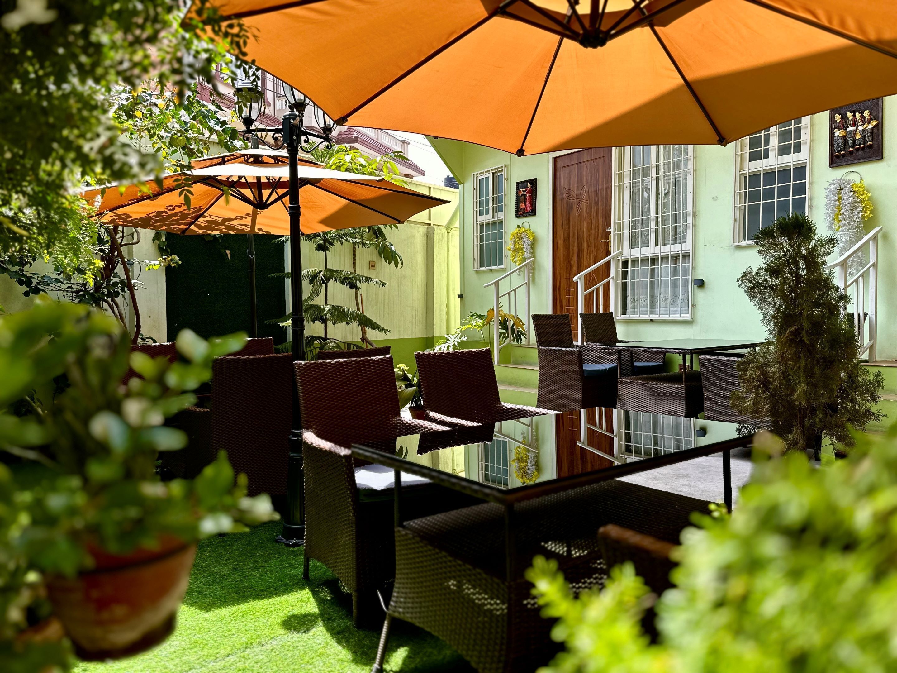An outdoor patio with wicker furniture, a glass table, and orange umbrellas providing shade.