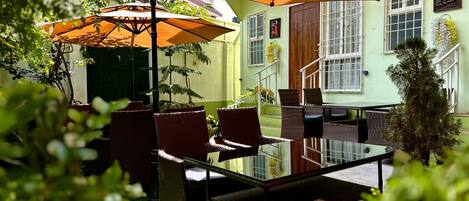 An outdoor patio with wicker furniture, a glass table, and orange umbrellas providing shade.