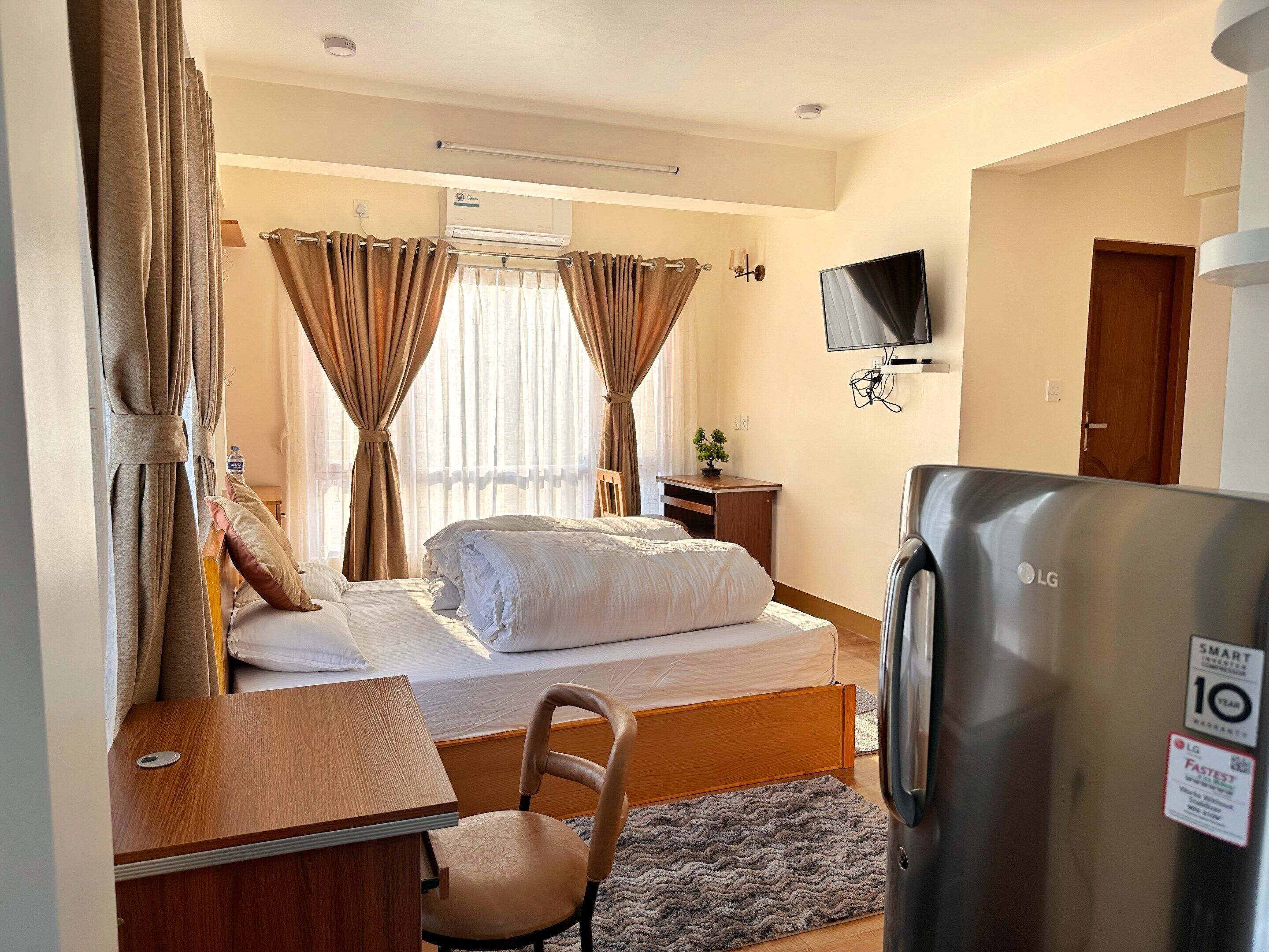 Ein Hotelzimmer mit Bett, Schreibtisch, Sessel, Fernseher und Kühlschrank.