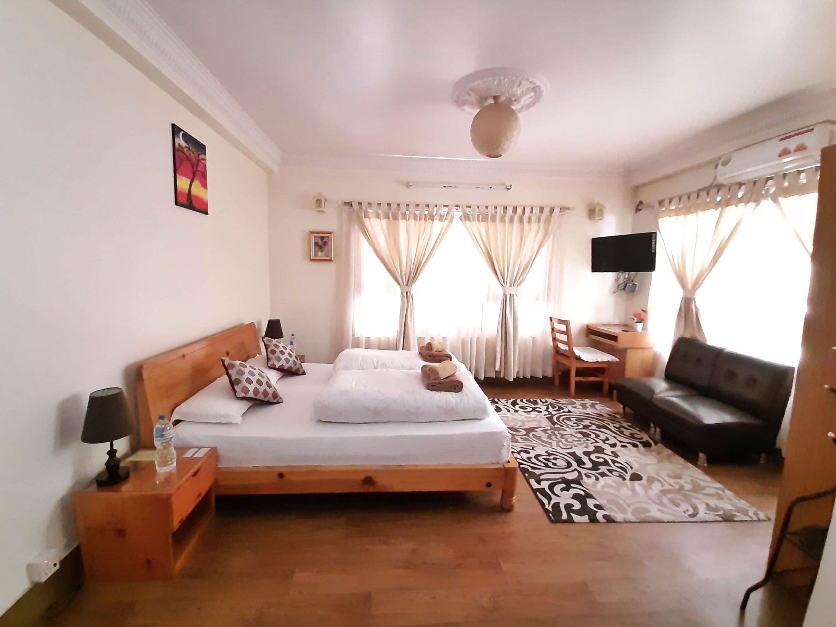Quarto com cama de madeira, escrivaninha, cadeira, sofá e televisão.