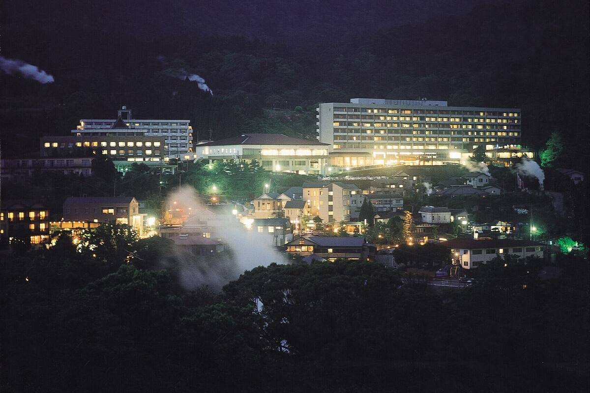 Ein Nachtblick auf eine Stadtlandschaft mit mehreren Gebäuden, darunter ein großes Hotel mit beleuchteten Fenstern.