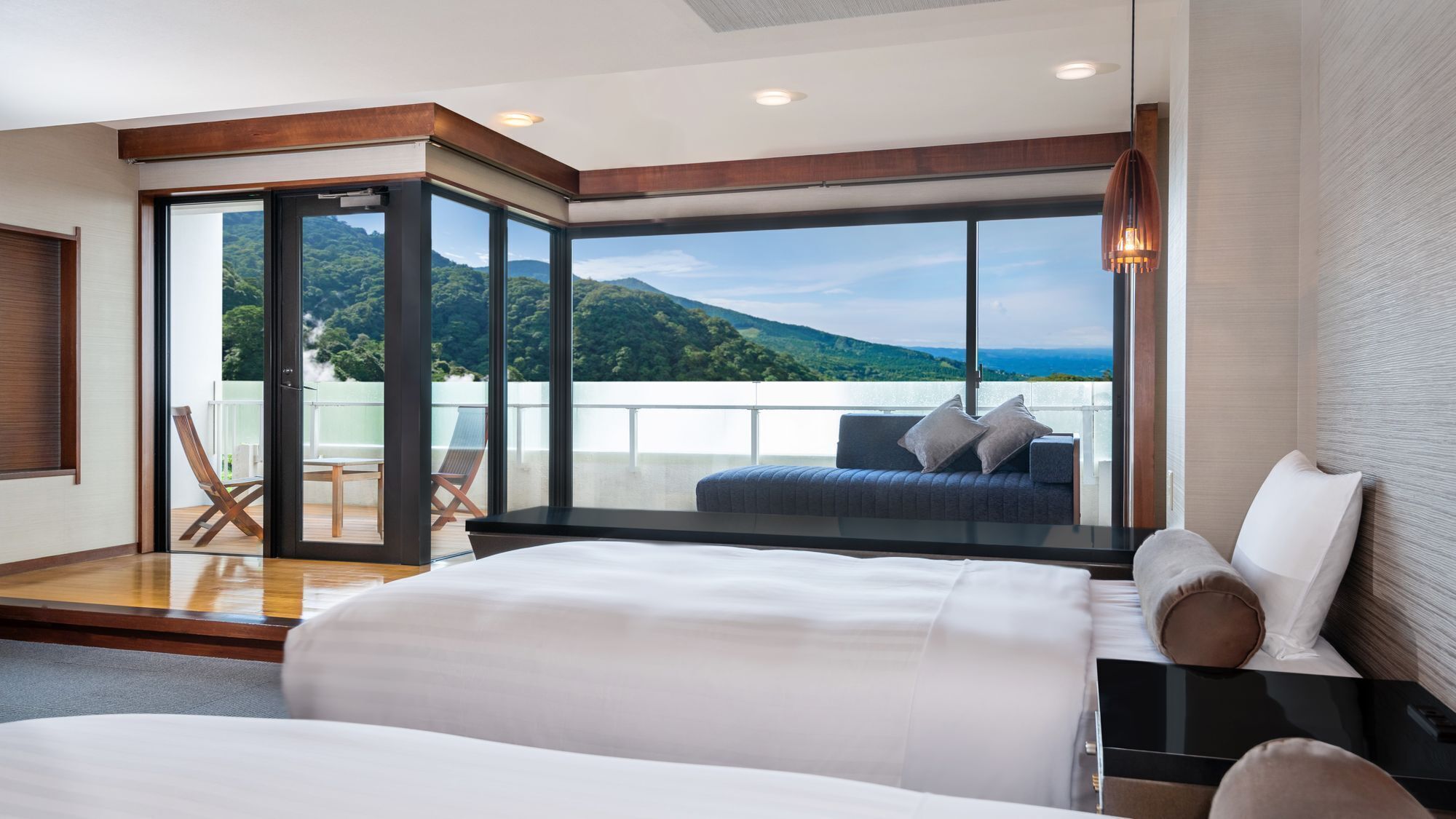 Une chambre d’hôtel moderne dotée d’un grand lit, d’un balcon offrant une vue sur les montagnes et d’un coin salon avec vue.