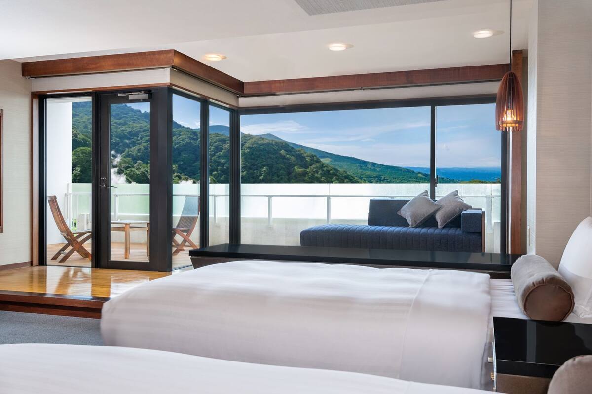 Ein modernes Hotelzimmer mit einem großen Bett, einem Balkon mit Bergblick und einer Sitzecke.