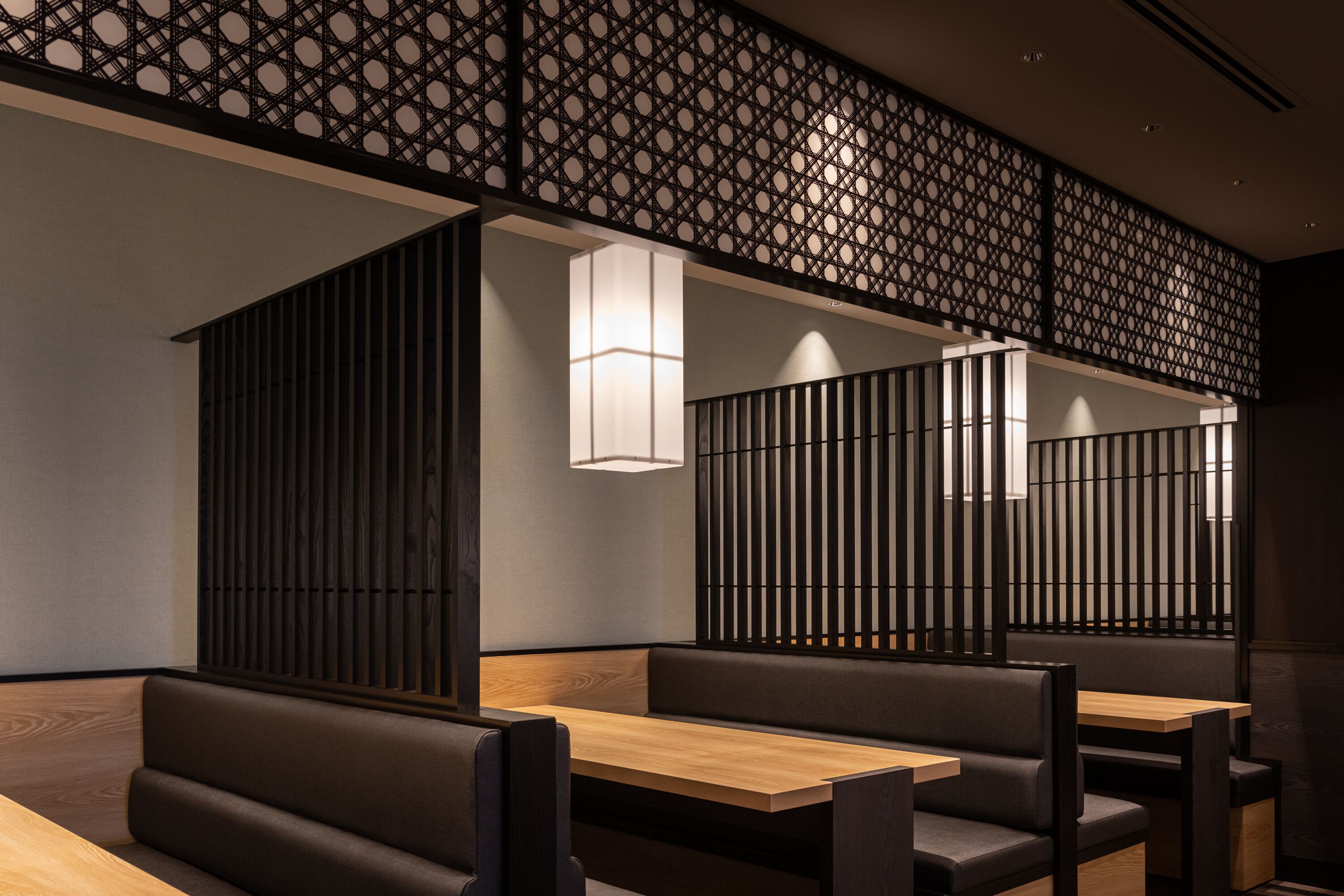 A modern interior with wooden tables and cushioned booths, featuring a geometric patterned ceiling and recessed lighting.