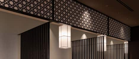 A modern interior with wooden tables and cushioned booths, featuring a geometric patterned ceiling and recessed lighting.