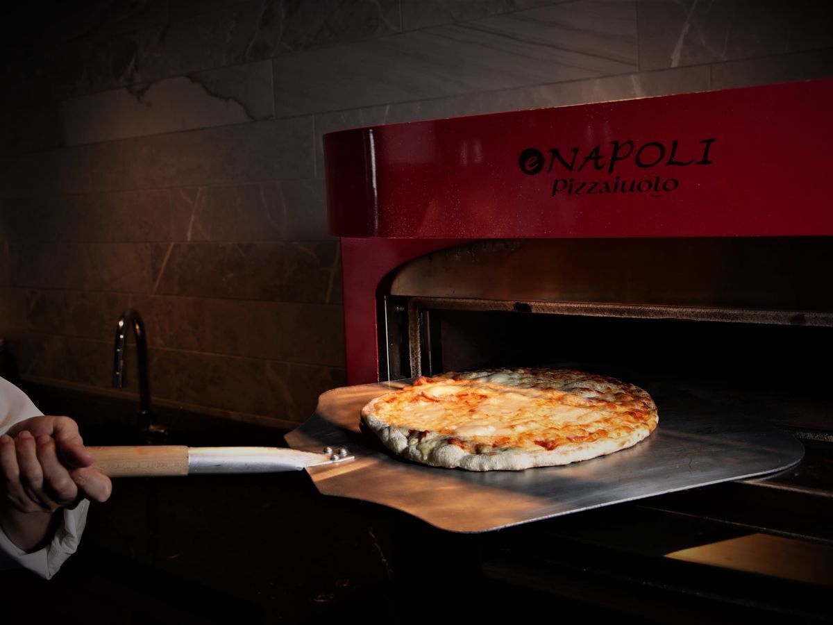 A pizza being removed from a red oven with the brand "NAPOLI PIZZA AUOLO" visible.