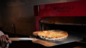 Una pizza siendo retirada de un horno rojo con la marca 'NAPOLI PIZZA AUOLO' visible.