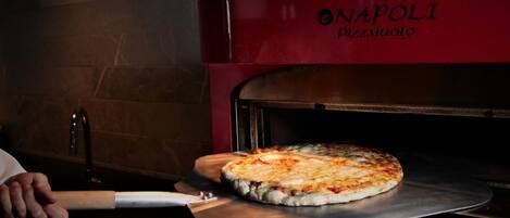 A pizza being removed from a red oven with the brand "NAPOLI PIZZA AUOLO" visible.
