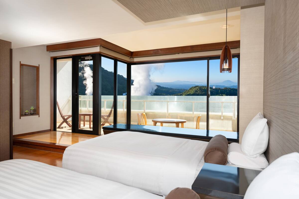 Ein modernes Hotelzimmer mit einem großen Bett, einem Balkon mit Bergblick und einer Schiebetür, die auf den Balkon führt.