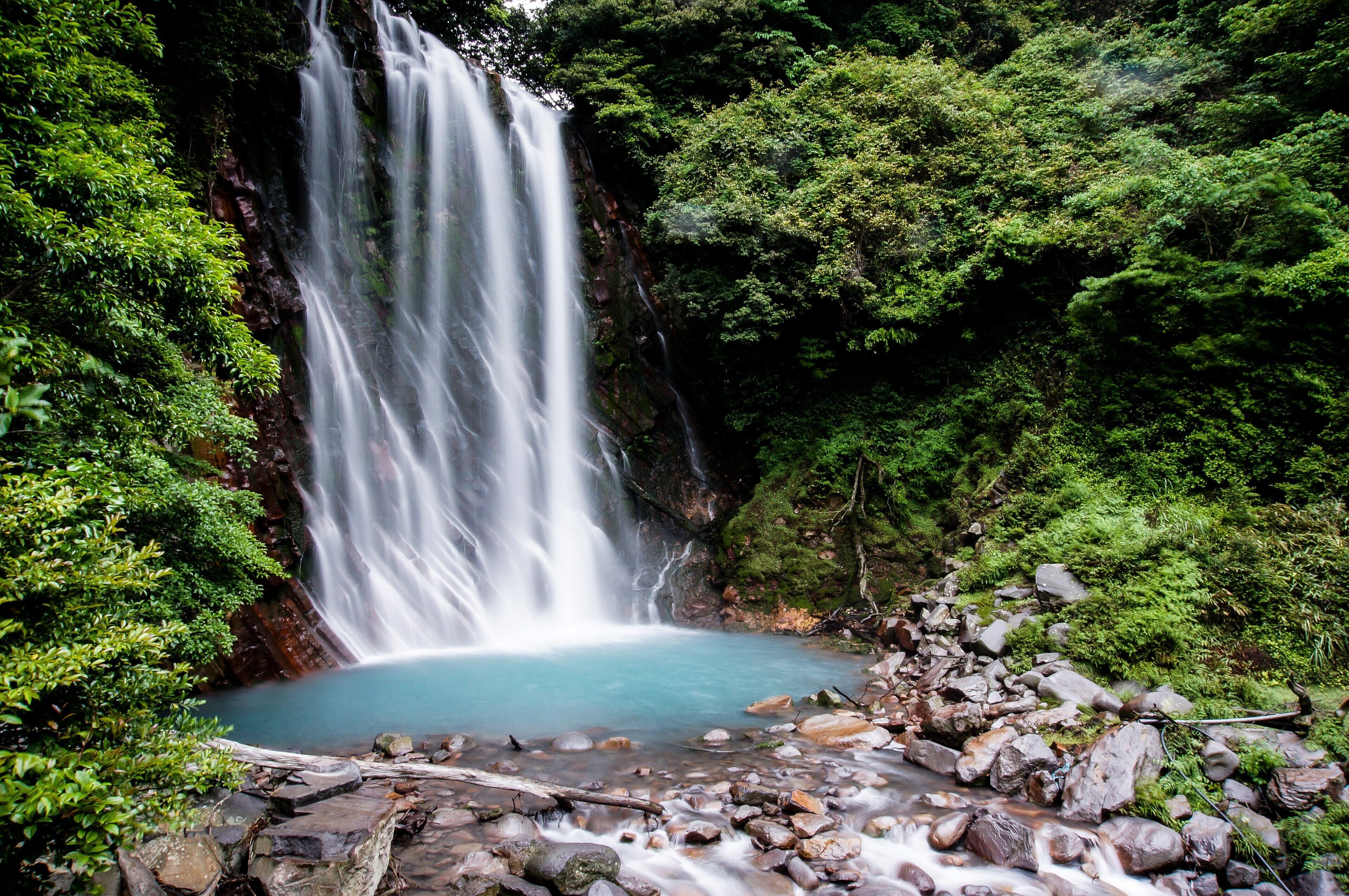 A waterfall cascading into a clear pool surrounded by rocks and lush greenery.