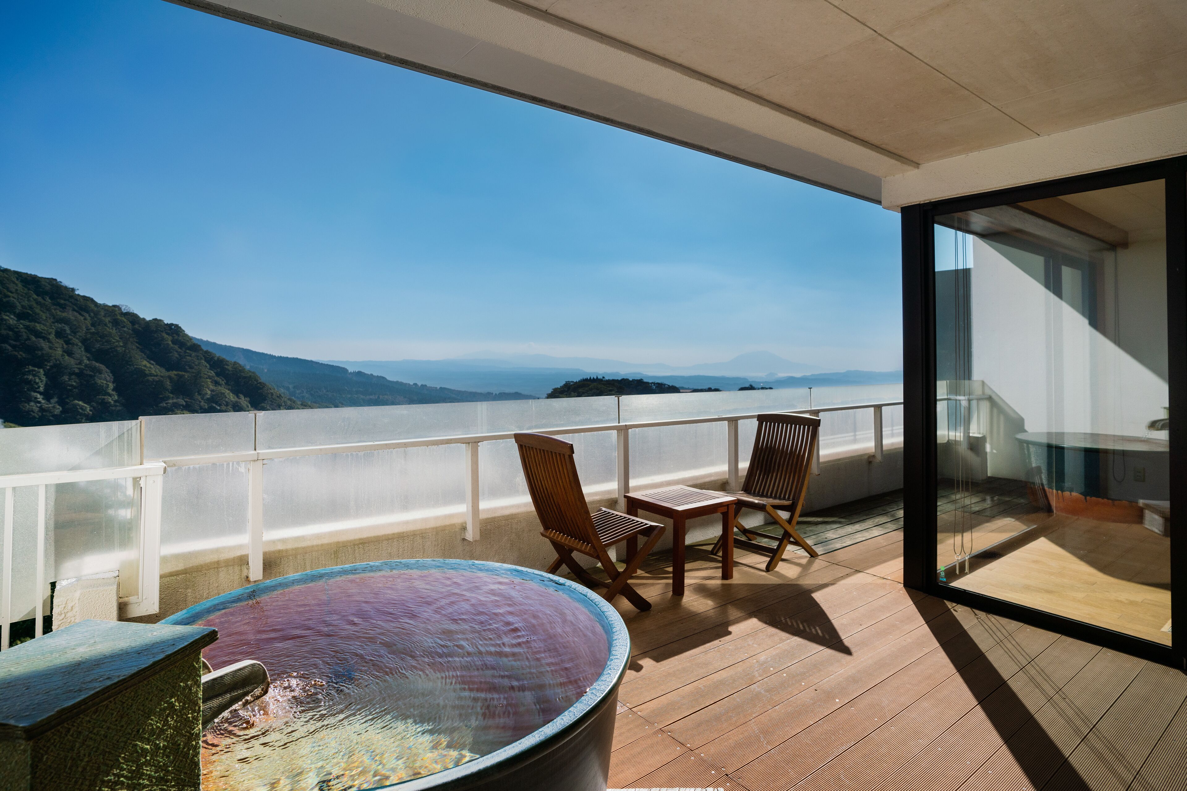 Un balcón con hidromasaje, dos sillas de madera y vistas a un paisaje montañoso.