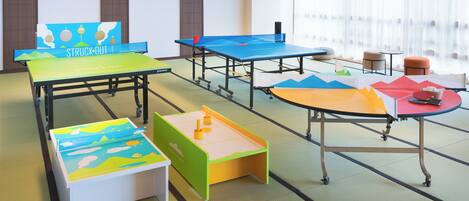 A room with tatami mat flooring, multiple ping pong tables, and a large projection screen.
