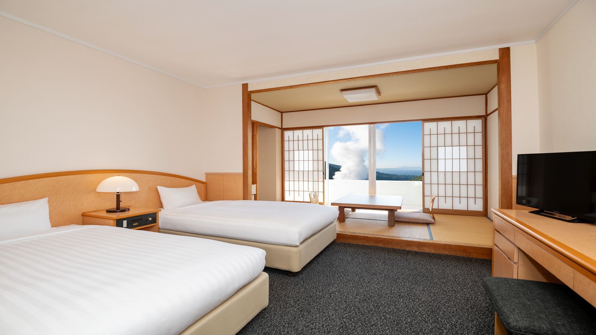 A hotel room with two beds, a TV, a desk, and a view of the mountains.