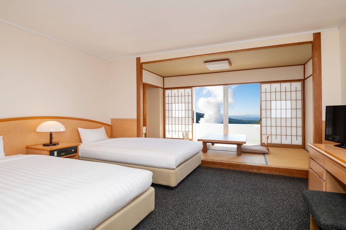 Ein Hotelzimmer mit zwei Betten, einem Fernseher, einem Schreibtisch und Blick auf die Berge.