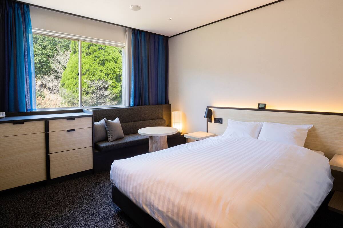 Ein Hotelzimmer mit einem großen Bett, einer Couch, einem kleinen Tisch und einem Schreibtisch mit Schubladen.