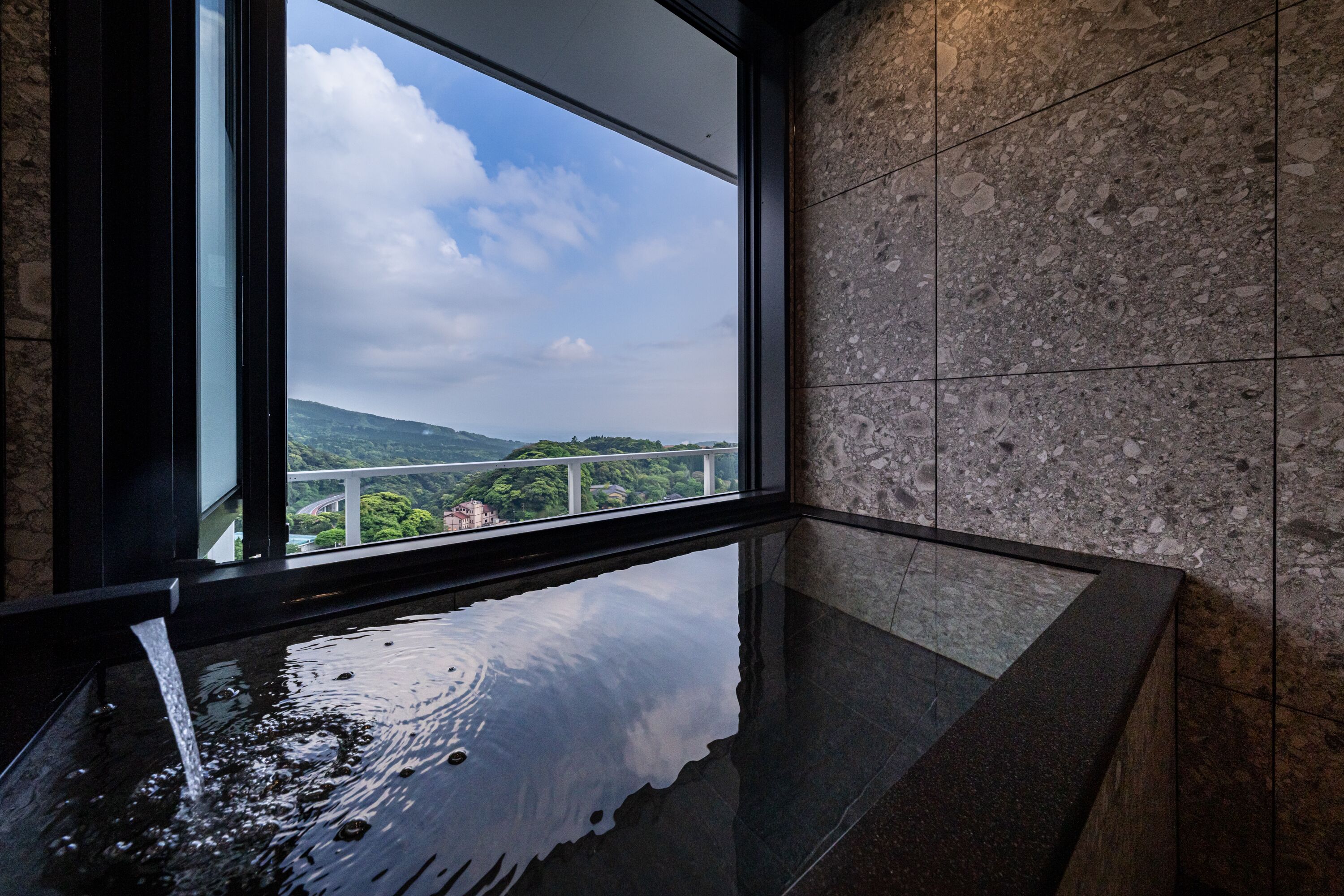 Une salle de bain moderne dotée d’une grande fenêtre, d’un élément décoratif aquatique et offrant une vue sur un paysage montagneux.