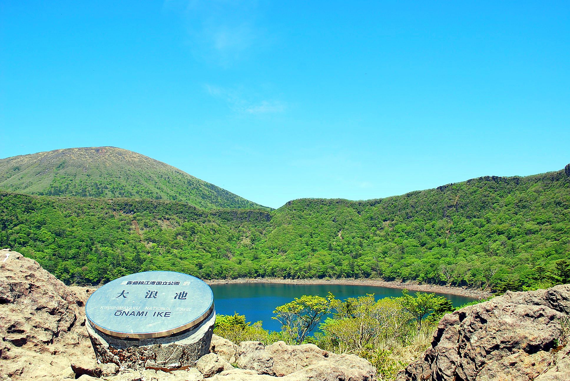 A view of Onami Ike National Park with a clear sky and a lake surrounded by green hills.