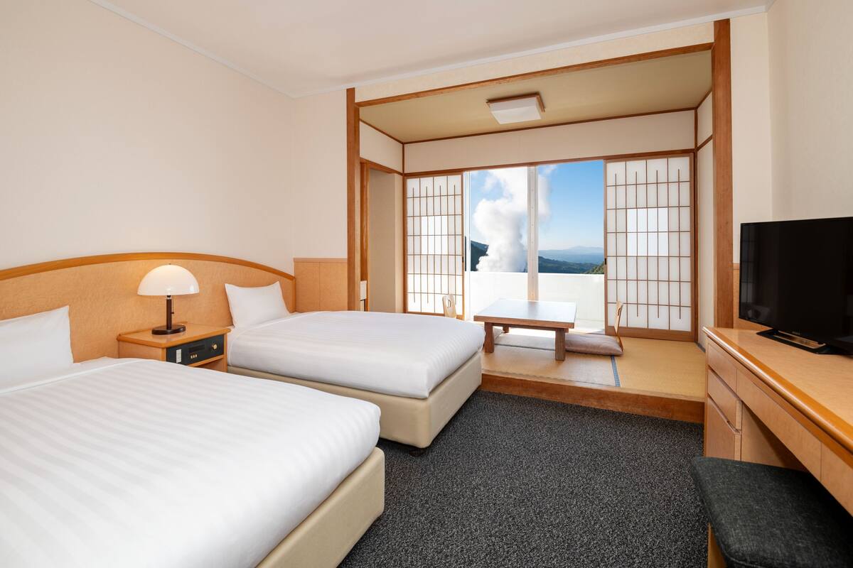 Ein Hotelzimmer mit zwei Betten, einem Schreibtisch, einem Fernseher und Blick ins Freie.
