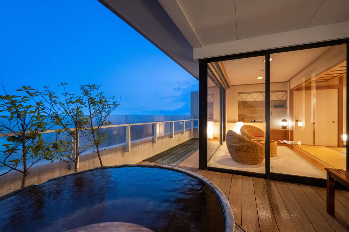Ein modernes Hotelzimmer mit einer großen Schiebeglasdoor, die auf einen Balkon mit Blick aufs Meer führt.