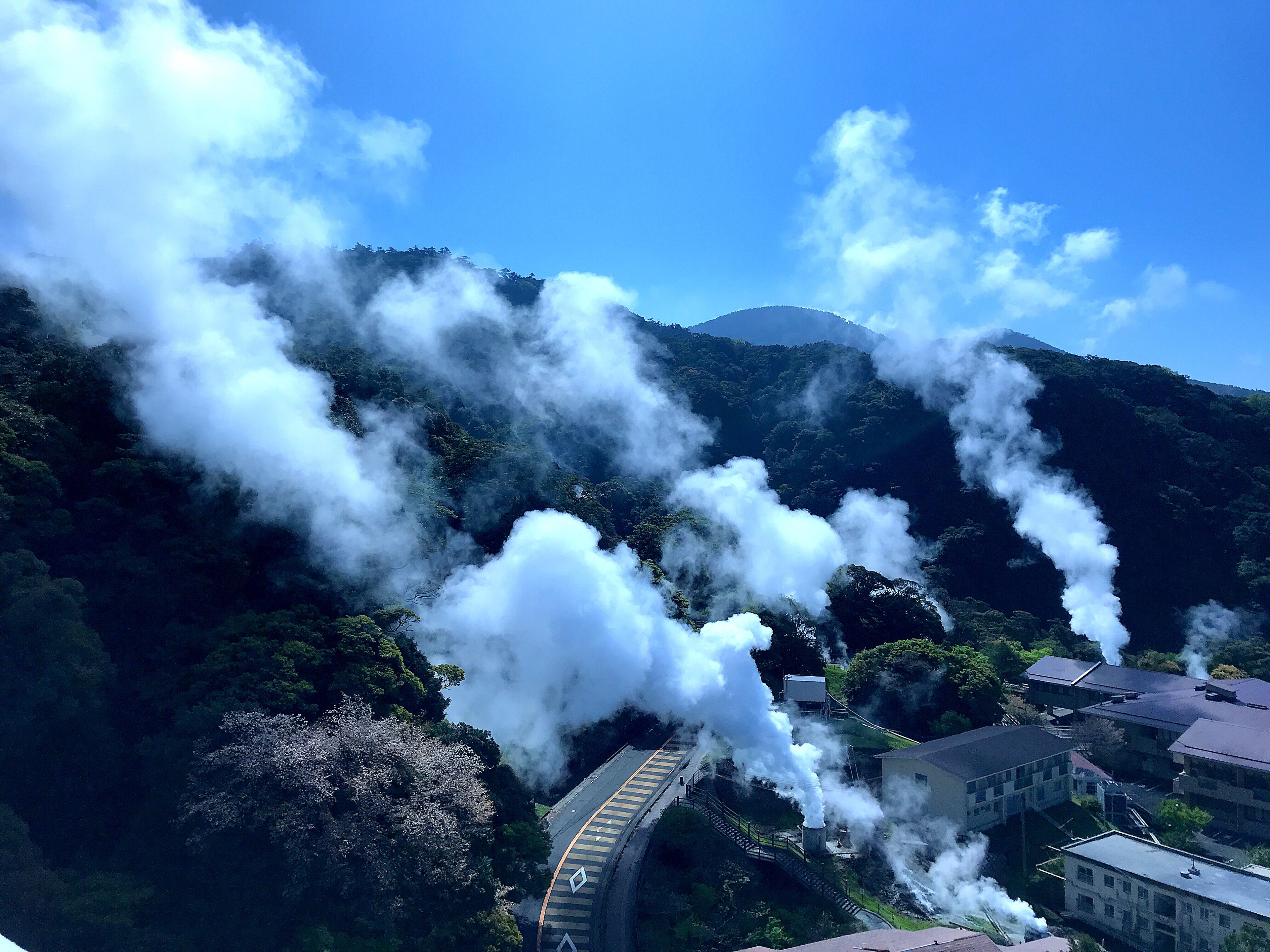 A train emitting steam through a tunnel, surrounded by lush greenery and a mountainous backdrop.